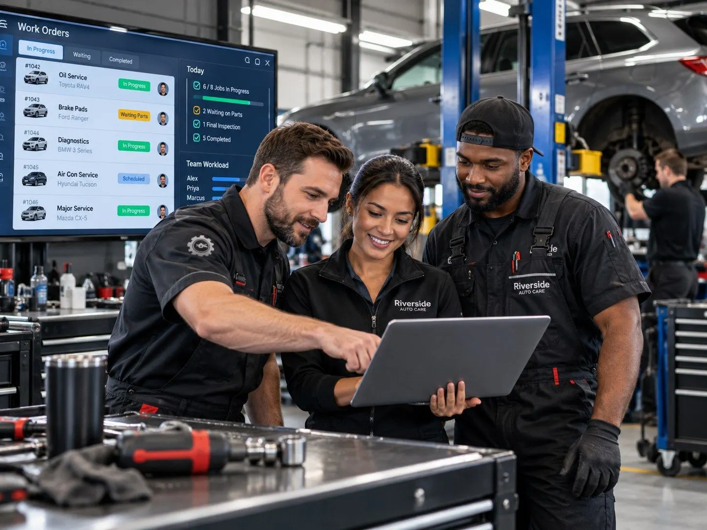 Three mechanics planning work orders on a laptop in the workshop
